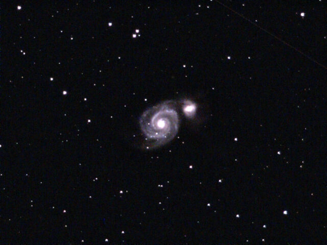 M51, appelée la galaxie du Tourbillon, est une galaxie spirale située à environ 27 millions d’années-lumière de la Terre, dans la constellation des Chiens de chasse. Avec un simple télescope, on peut distinguer sa forme caractéristique en spirale, très semblable à celle de notre propre Voie lactée. Ce qui la rend encore plus remarquable, c’est sa petite galaxie voisine, NGC 5195, qui semble être aspirée par l’attraction gravitationnelle de M51. Cette interaction provoque des déformations et stimule la naissance de nouvelles étoiles dans les bras spiraux. Observer M51, c’est donc avoir sous les yeux un exemple saisissant de l’évolution des galaxies dans l’Univers.